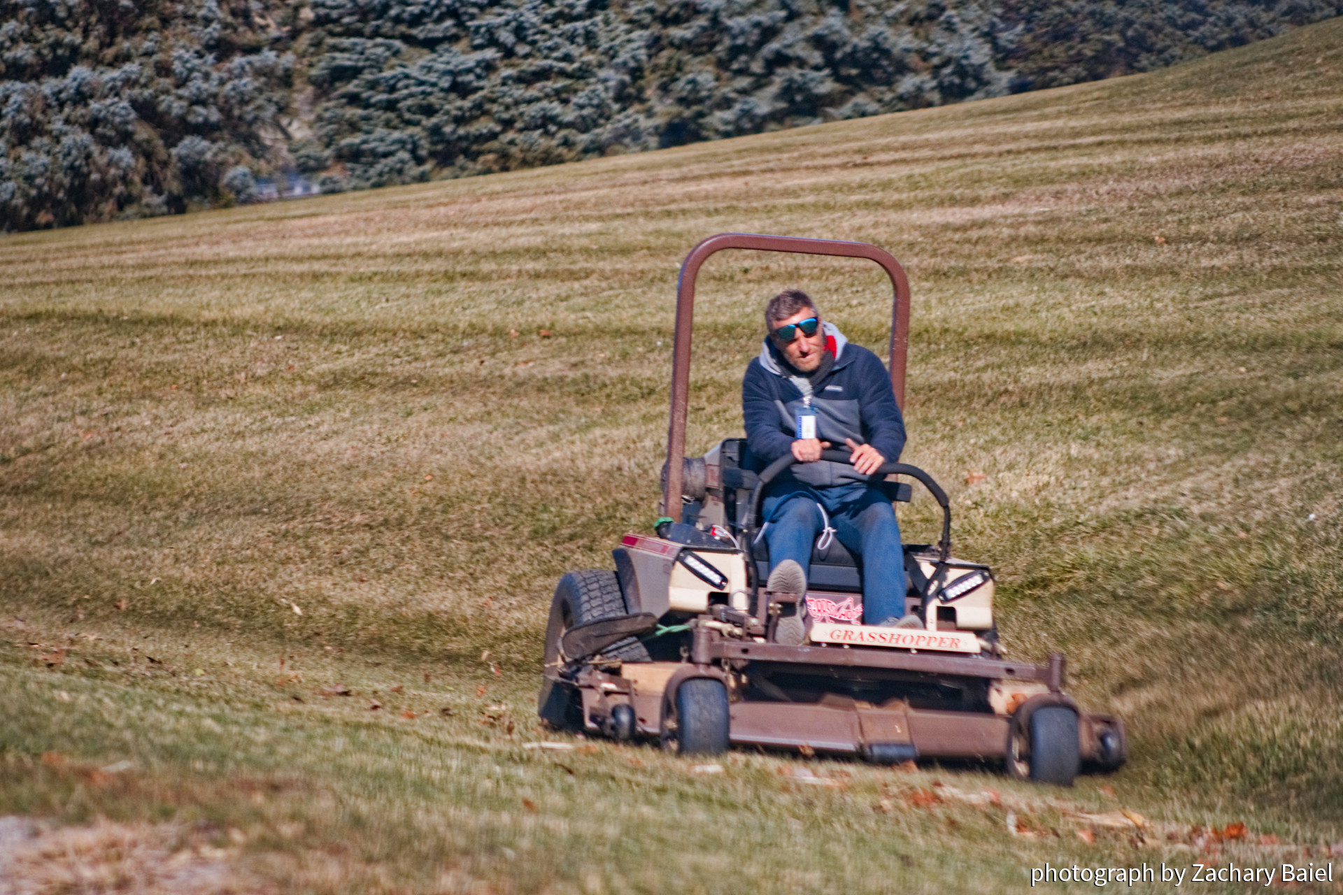 Groundskeeper on a riding lawn mower, completing the final mow around a school | November 2022